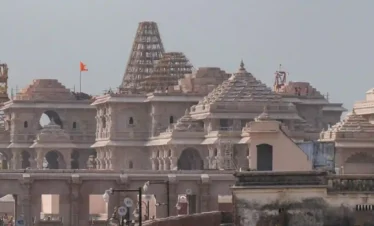The Ram Janmabhoomi temple under construction in Ayodhya, featuring detailed stone architecture, tiered domes with scaffolding, and a saffron flag.