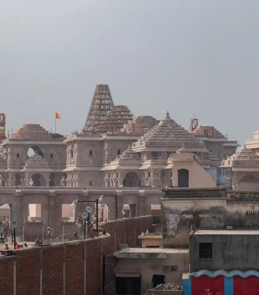 The Ram Janmabhoomi temple under construction in Ayodhya, featuring detailed stone architecture, tiered domes with scaffolding, and a saffron flag.
