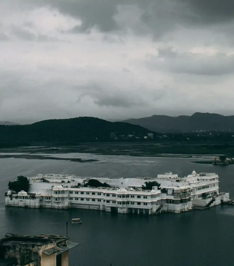 Elegant white marble palace floating on Lake Pichola with scenic hills and cloudy sky in Udaipur.