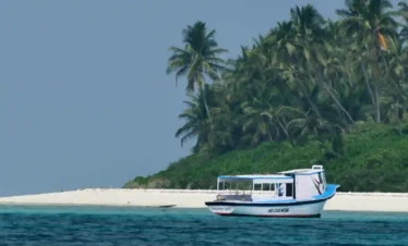 Agatti Island, Lakshadweep – a small boat cruising over clear blue waters near a pristine white sand beach lined with lush coconut palms, showcasing a peaceful tropical island escape.