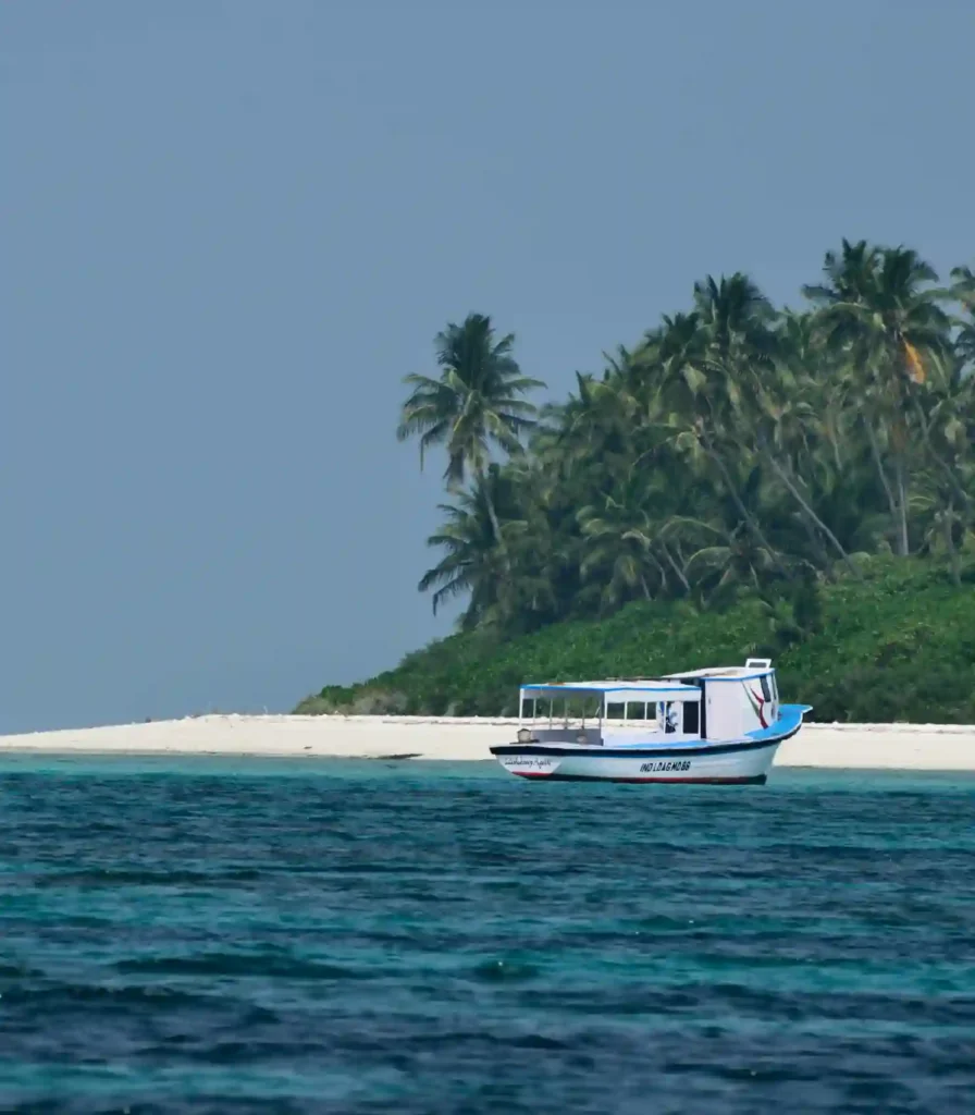 Agatti Island, Lakshadweep – a small boat cruising over clear blue waters near a pristine white sand beach lined with lush coconut palms, showcasing a peaceful tropical island escape.