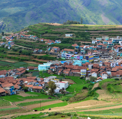 A vibrant village with colorful houses clustered on a terraced green hillside in a mountainous region.